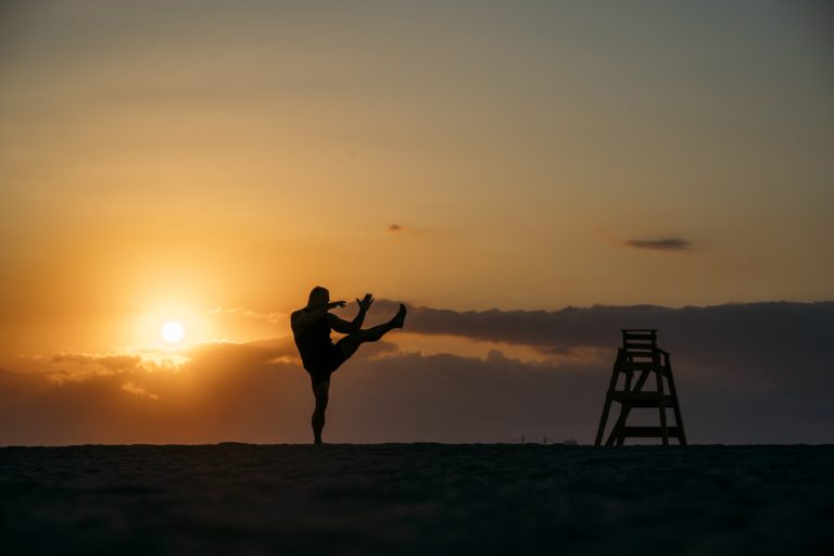 Silhouette of man practicing martial arts on beach.